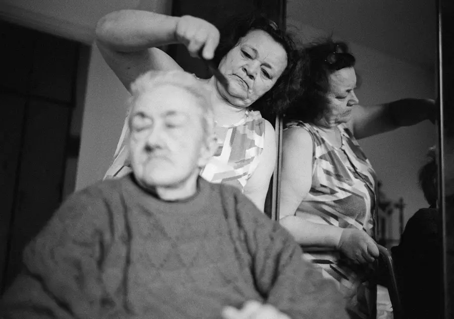 Darya combs Ottilia's hair just after she's released from the hospital after being diagnosed with in-operable pancreatic cancer. Ottilia is 86 years old. Darya, a remarkable, 54 year-old woman from the Ukraine, has been working as a \\\"badante\\\" (caretaker for the elderly) for the last five years in Bolzano, Italy. Darya takes care not of one, but four sisters - Augusta, 94, Gisella, 84, Elena, 77, and Ottila, 86. She lives in the small apartment with the women, sleeping on a fold-out sofa in the living room. The sisters are severely handicapped, with Parkinson's disease, Alztheimer's, blindness, and cancer. They all wear diapers and two are unable to walk. They have no teeth and two must be hand-fed. Darya takes care of everything - washing, dressing, feeding each woman, everyday, 7 days a week, as well as all the cleaning and laundry and grocery shopping that these women require. She has only 3 hours off in the afternoon, at which time she cleans the apartments of two other people, for cash and off the books. On Sundays she uses her hours off to go to mass. Darya is deeply religious and prays every morning and every night. She sends all the money she earns to her husband and two daughters who wait for her in a tiny village in Ukraine. She goes home only once a year, usually in August. Darya is one of thousands of Ukrainian women who work in Italy like this, far from home, taking care of other peoples' dying parents. Bolzano, Italy, 2007.
